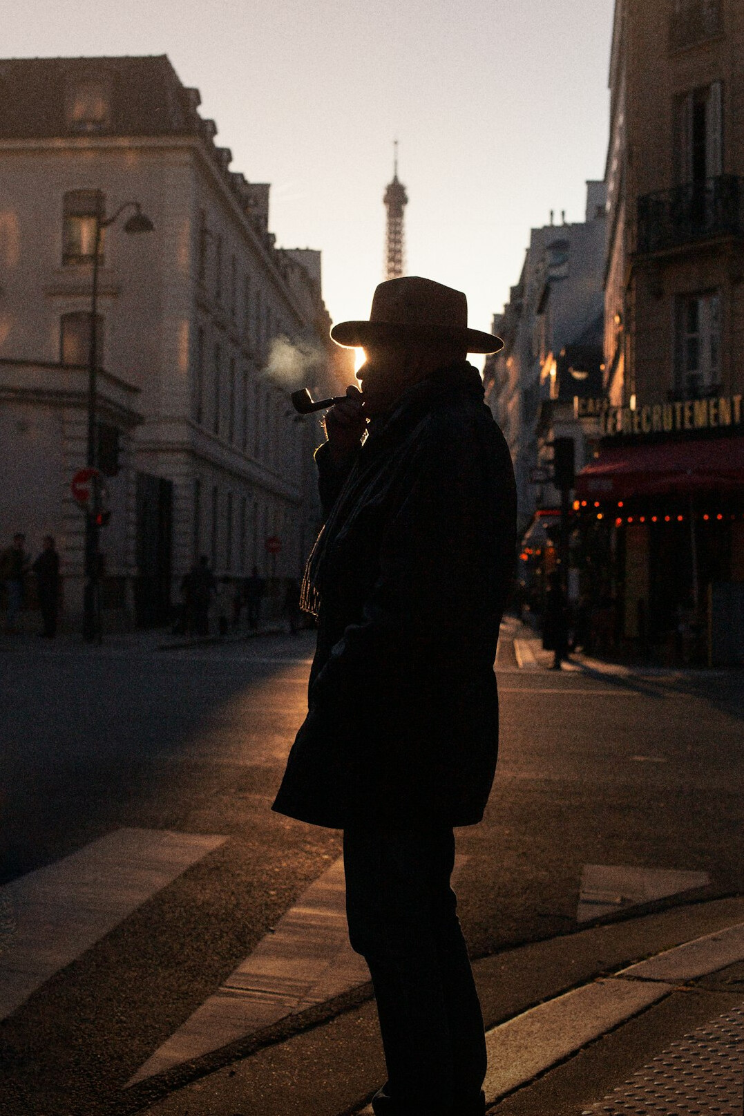 Silhouette of a man in a coat and hat standing under a streetlamp